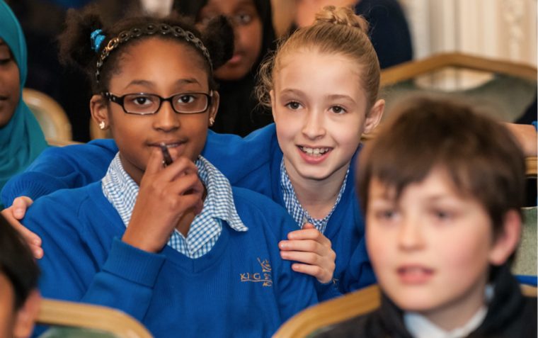 Three primary school pupils (a boy and two girls) sitting inside a classroom.