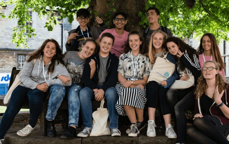A group of Debate Academy students (male and female) sitting under a tree outside the building.