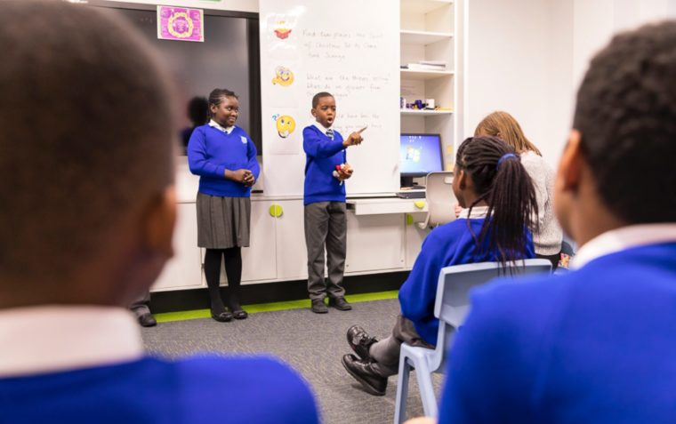 two children in blue sschool uniform presenting to class in a classroom