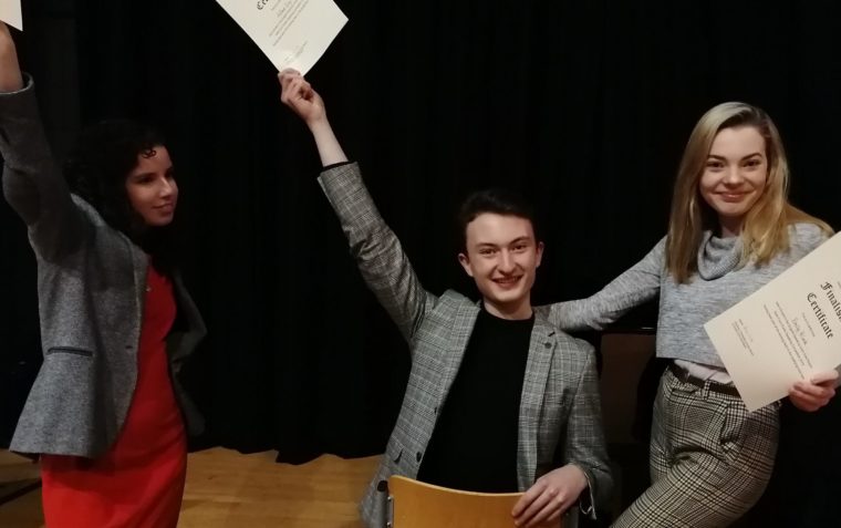3 students, one boy on a chair and two girls standing, posing with their finalist certificate