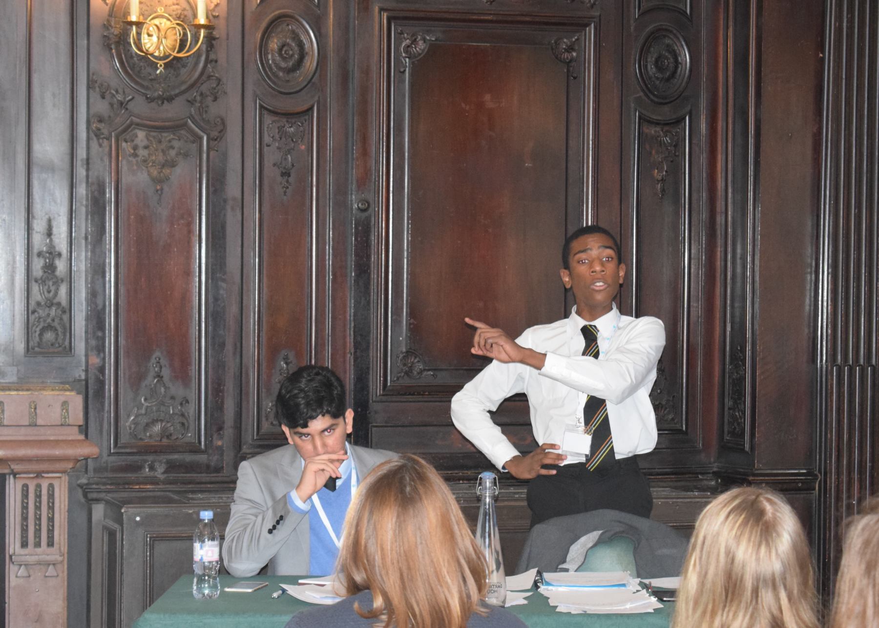 A young pupil passionately delivers his speech while his team mate is writing down his notes