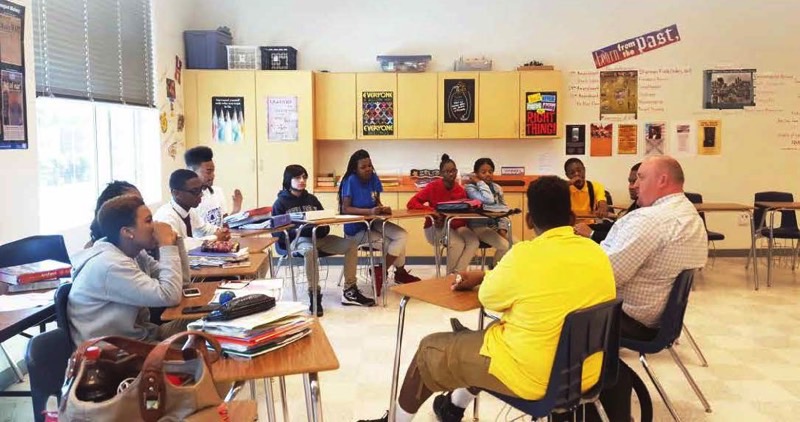A group of secondary school students (male and female) sitting in a semi-circle inside a classroom. 