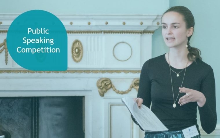 An image of a female standing and speaking during with a notepad in her hand and has Public Speaking Competition written on it.