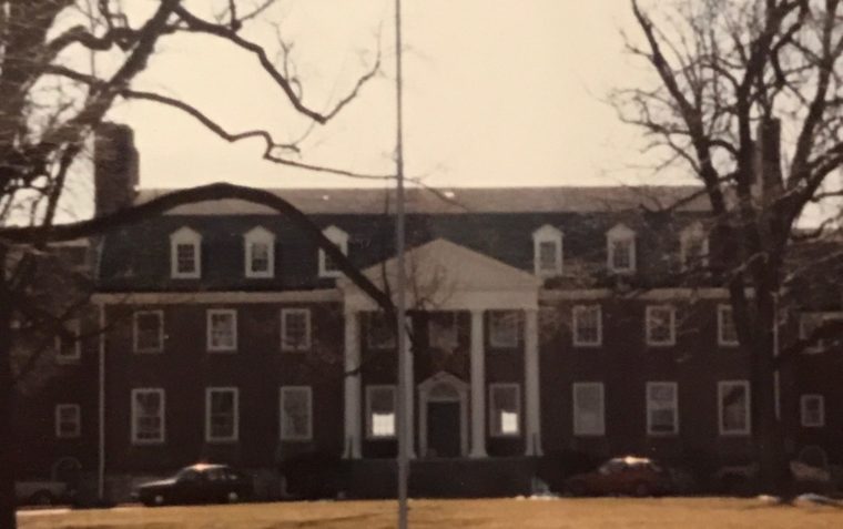 A picture of the front building of Saint James Secondary School in Maryland, USA with two dry trees and USA flag in the front yard.