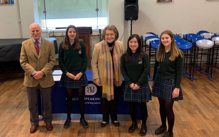 A photograph of three female students of South Wiltshire Grammar School along with an old man and an old woman standing in front of a registration table inside a hall.