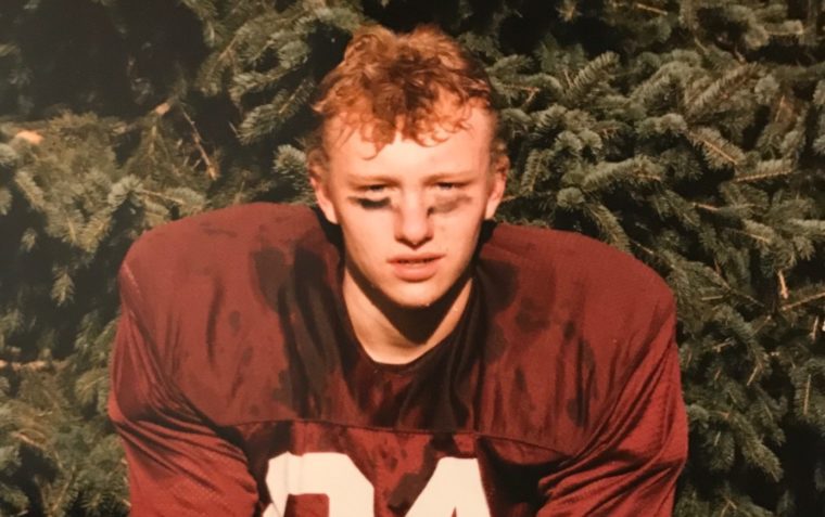 A picture of Mark Mortimer as a teenager in American Football kit with heap of bush in the background.